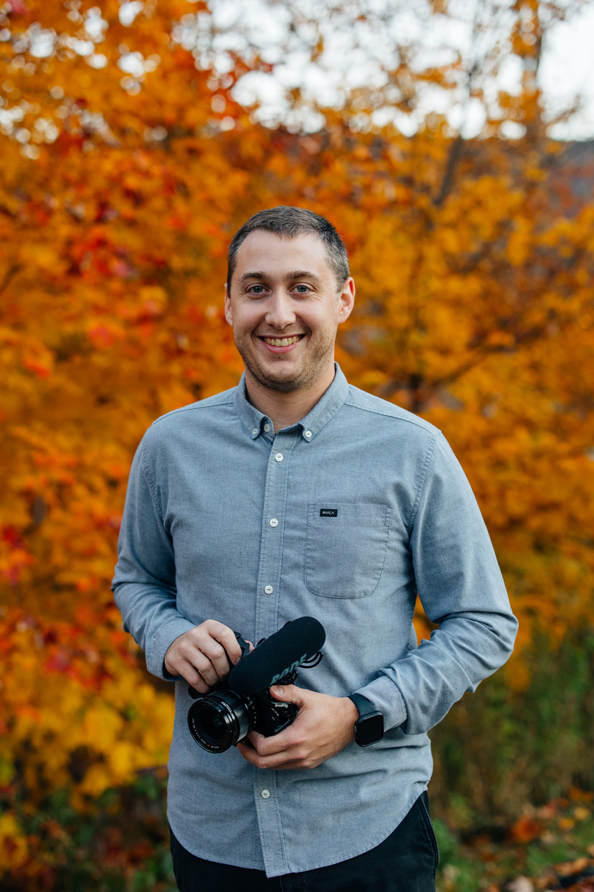 Brian Reubelt of Ledge Light Films holding a camera rig against autumn foliage